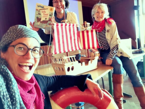 Katharina Mauder, Yvonne Hergane und Karin Baron in Piraten-Outfits mit einem Holzschiff und dem großen Elbautor:innen Vorlesebuch "Volle Fahrt voraus!"