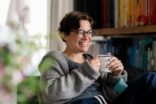 Katharina Mauder lacht beim Kaffeetrinken neben guten Bilderbüchern