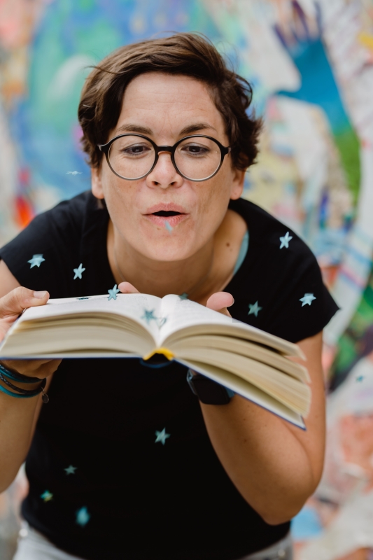 Die Kinderbuchautorin Katharina Mauder pustet Sternchen-Konfetti von einem Buch in die Welt